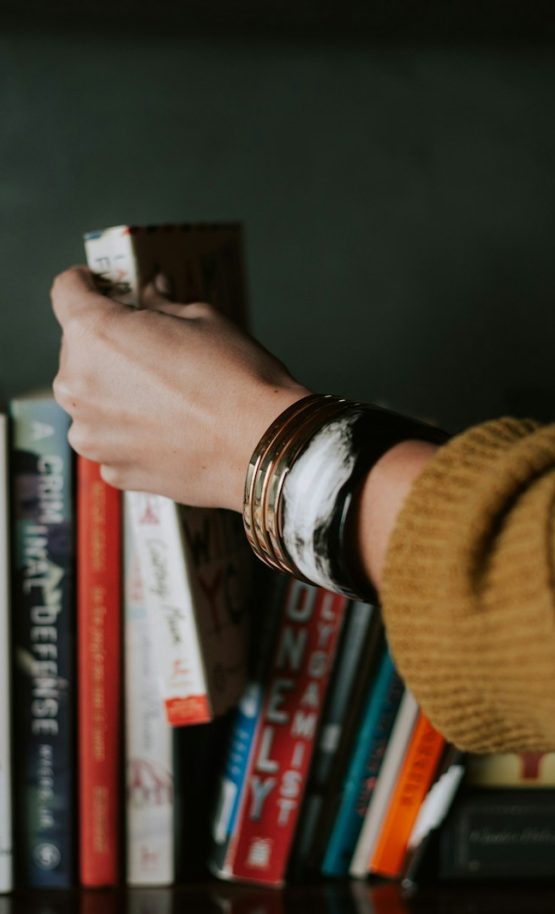 person picking white and red book on bookshelf {{brizy_dc_image_alt imageSrc=